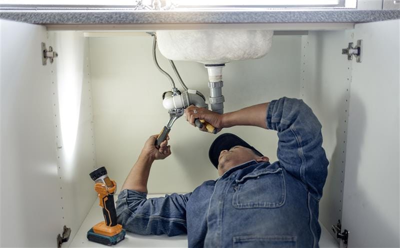 Plumber repairing pipes beneath a bathroom sink in West Jordan
