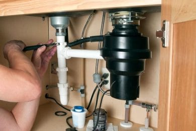 Plumber repairing a garbage disposal beneath a kitchen sink in West Jordan