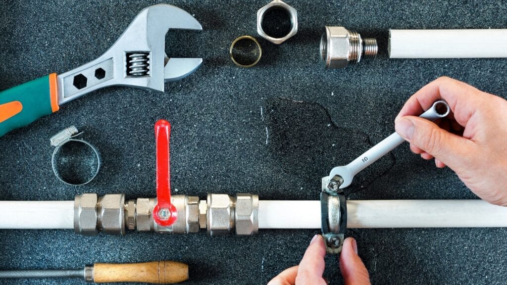 Plumber repairing a pipe valve with an adjustable wrench in West Jordan
