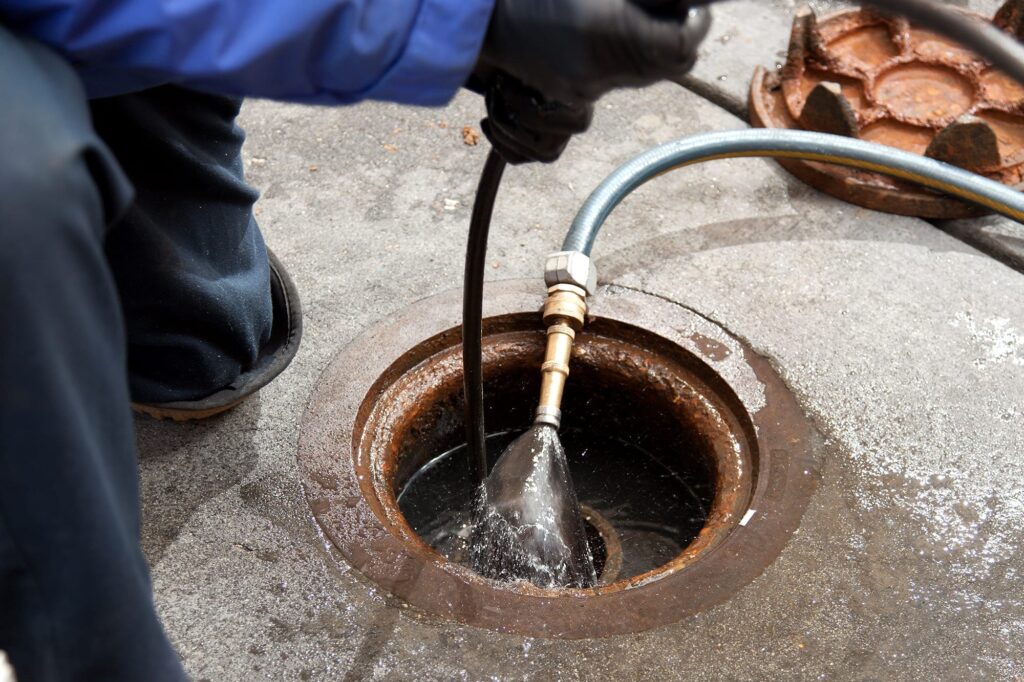 Plumber hydro jetting a sewer line through a manhole in West Jordan