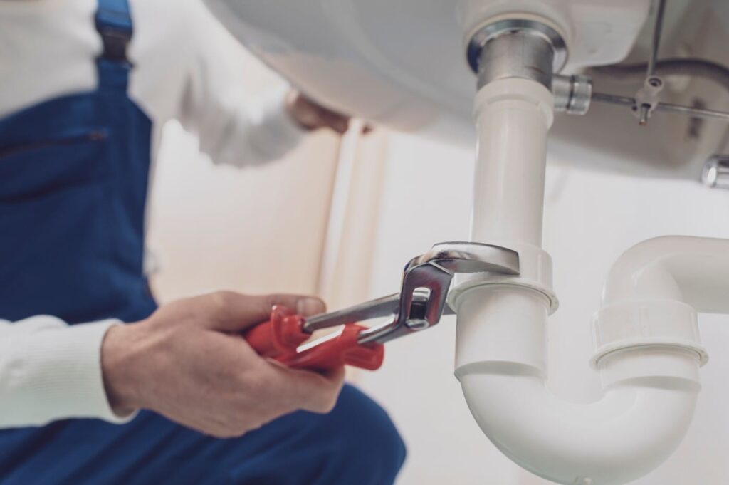 Plumber repairing a white drain pipe beneath a sink in West Jordan