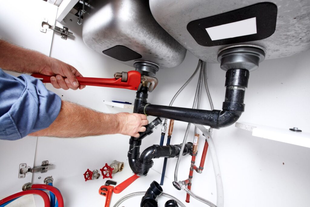 Plumber repairing drain pipes beneath a kitchen sink in West Jordan