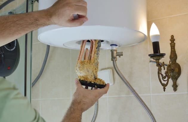 Technician removing mineral buildup from a water heater in West Jordan